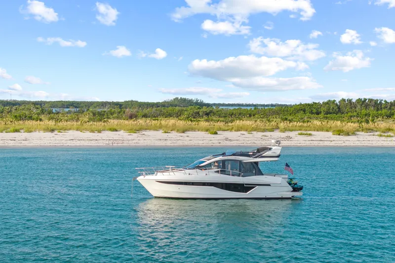 Good Vibes Yacht Photos Pics 2022 Galeon 470 Sky yacht on serene blue water near a sandy beach.