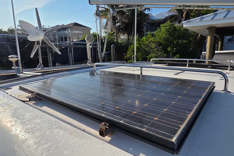 Beshert Yacht Photos Pics Solar panel on 2004 Leopard 47 catamaran, with wind turbine, docked near greenery.