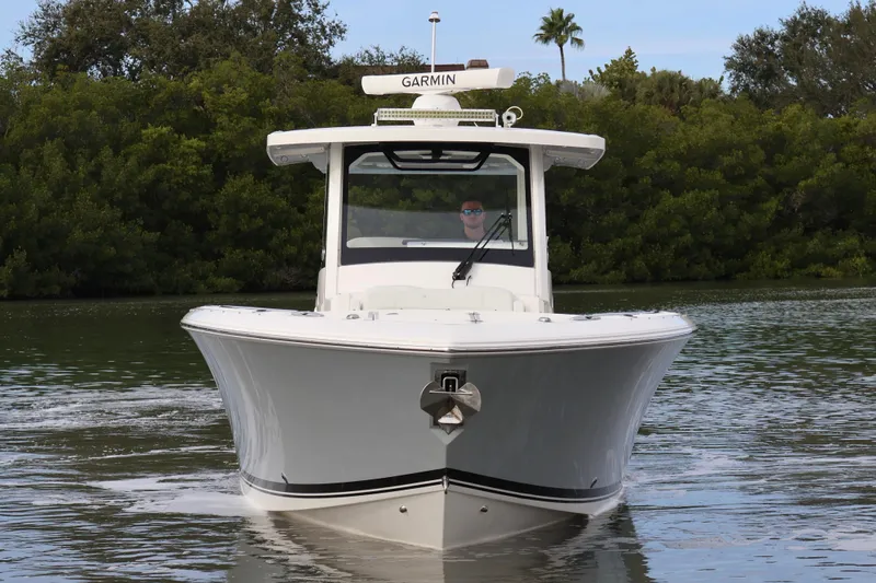  Yacht Photos Pics 2021 Pursuit S 328 Sport boat on calm water, surrounded by lush greenery.