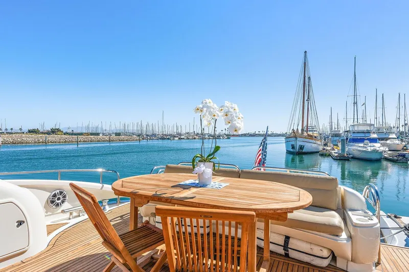 Blue Steel Yacht Photos Pics Sunseeker Predator 80 yacht deck with wooden table, marina view, and clear blue sky.
