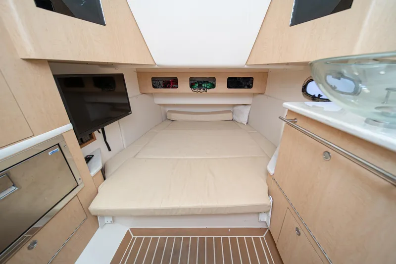 Vaquero Chingon Yacht Photos Pics 2016 Boston Whaler 370 Outrage cabin interior with bed, TV, and wooden cabinetry.