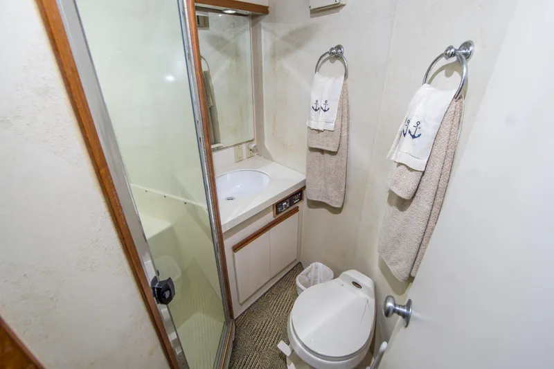 Aquila II Yacht Photos Pics Bathroom interior of 1990 Bertram 50 Convertible yacht with shower, sink, and nautical-themed towels.