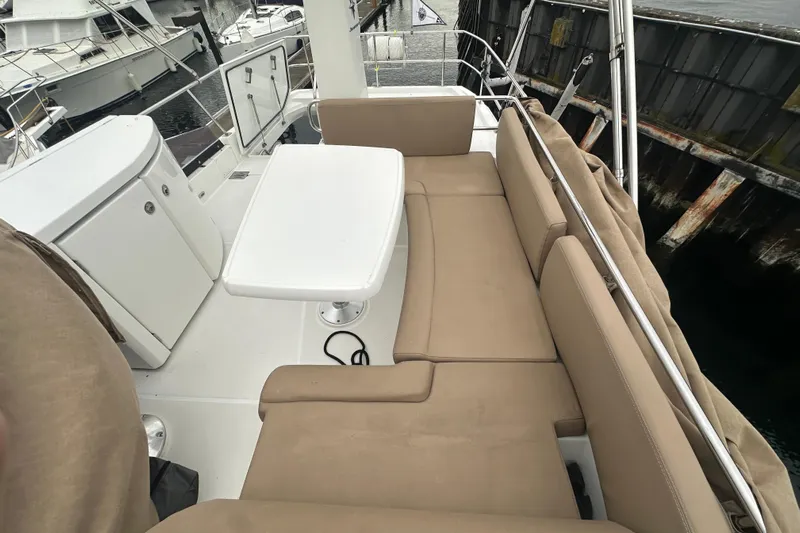 Couples Therapy Yacht Photos Pics Flybridge seating area on a 2014 Jeanneau Velasco 43 yacht, featuring beige cushions and a white table.