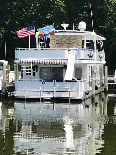 St. Somewhere Yacht Photos Pics 2017 Sumerset houseboat docked with flags and slide, reflecting on calm water.