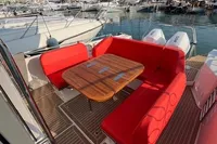 Red seating area on 2023 Nimbus T 11 boat with wooden table, docked at marina.