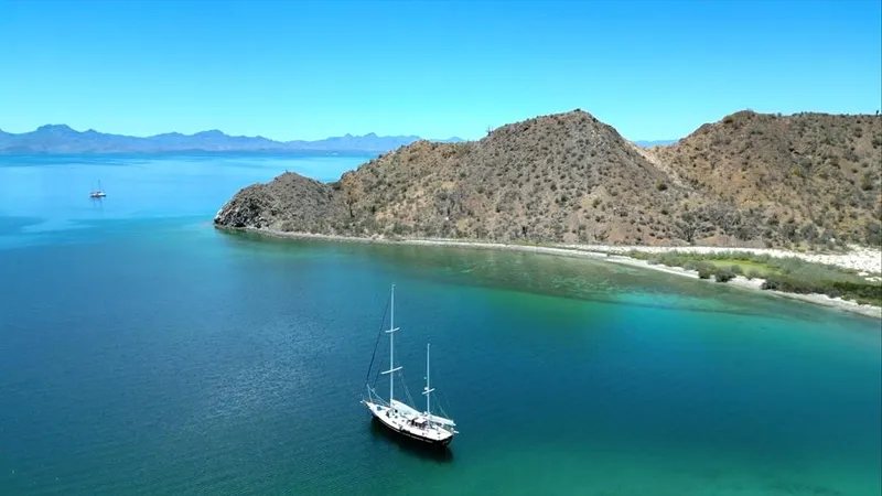  Yacht Photos Pics Sailboat anchored in clear blue waters near rocky coastline, Irwin Cutter Ketch 1984.