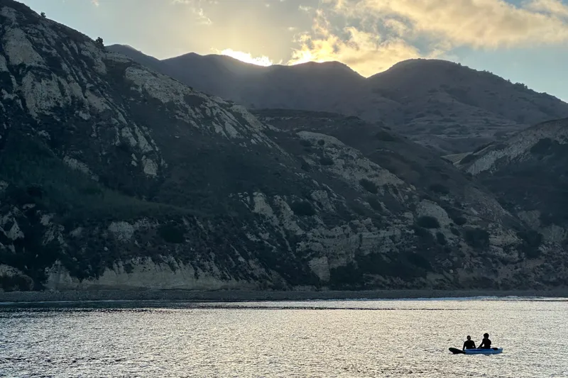  Yacht Photos Pics Two people in a small boat at sunset near rocky cliffs.