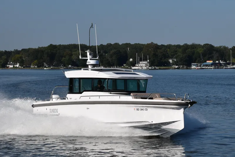 Sundog Yacht Photos Pics 2023 Axopar 37XC Wet Bar cruising on a serene lake with lush green shoreline.