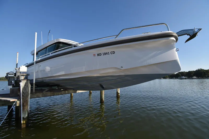 Sundog Yacht Photos Pics 2023 Axopar 37XC Wet Bar boat on lift over water, clear sky background.