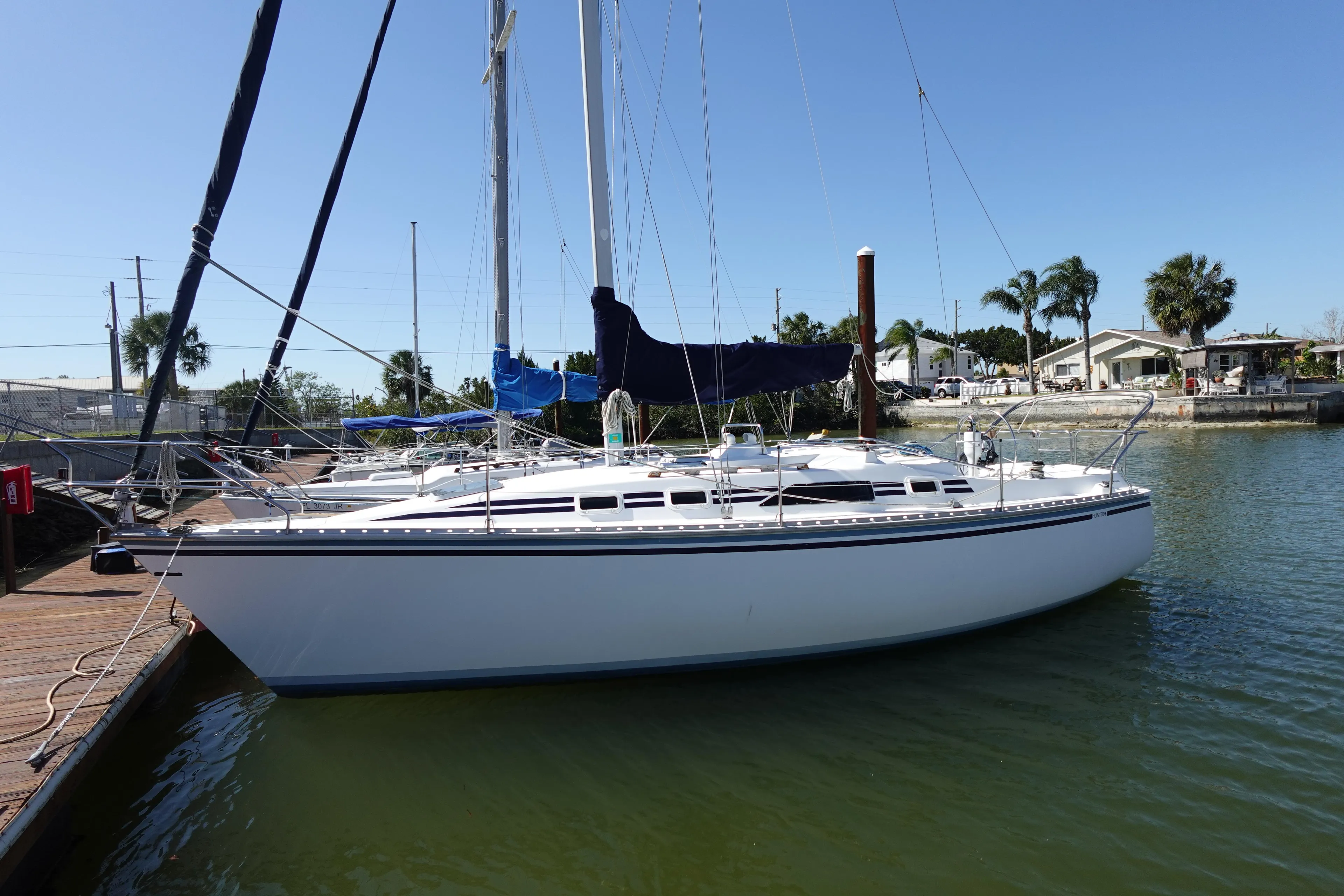 1987 Hunter 310 sailboat docked in a sunny marina with palm trees.