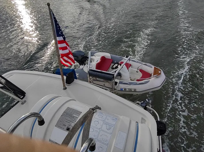 Snowy Owl Yacht Photos Pics Nordic Tug 42 (2000) with American flag and small boat in tow on water.