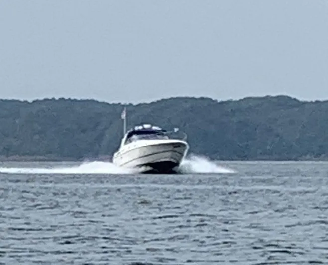  Yacht Photos Pics 2000 Cruisers Yachts 4270 Express speeding on water with forested background.