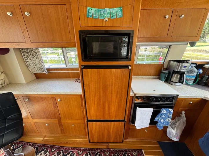 Eirene Yacht Photos Pics 2001 Mainship 390 kitchen with wooden cabinets, microwave, and stove, featuring a cozy interior design.