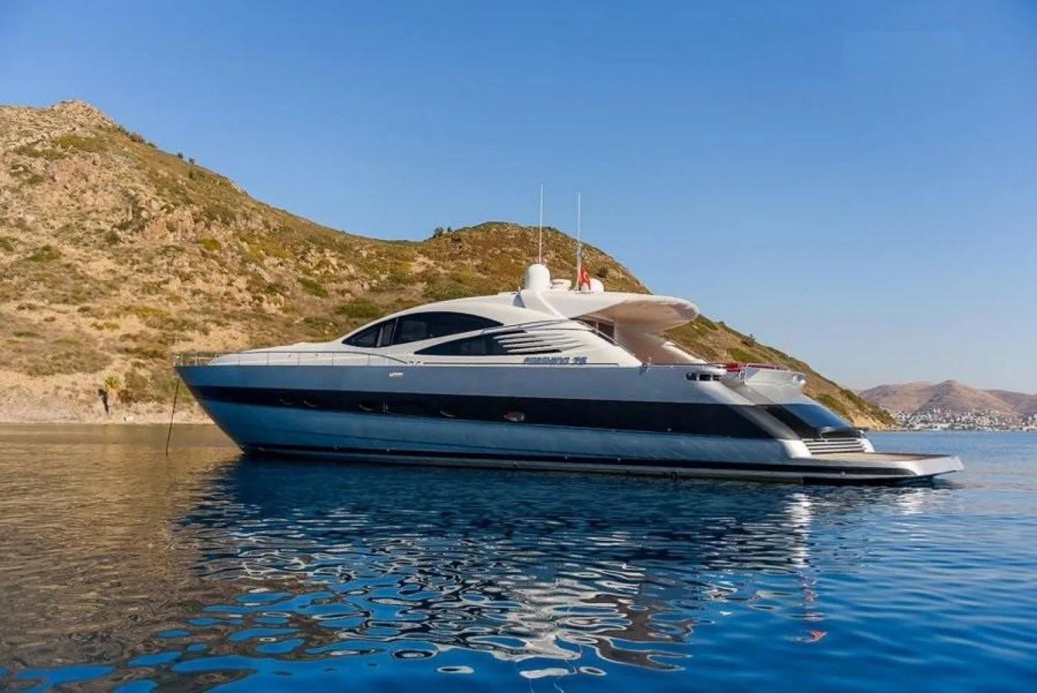 2005 Pershing 76 yacht on calm water near rocky coastline.