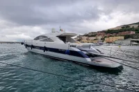 Luxury 2005 Pershing 76 yacht docked in a scenic harbor under cloudy skies.