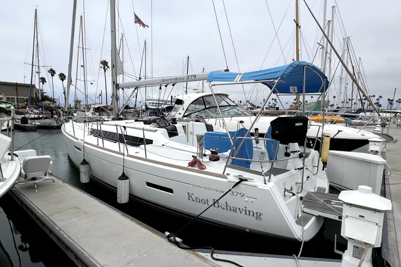 Knot Behaving Yacht Photos Pics 2014 Jeanneau Sun Odyssey 379 sailboat docked in marina, featuring blue canopy and sleek design.