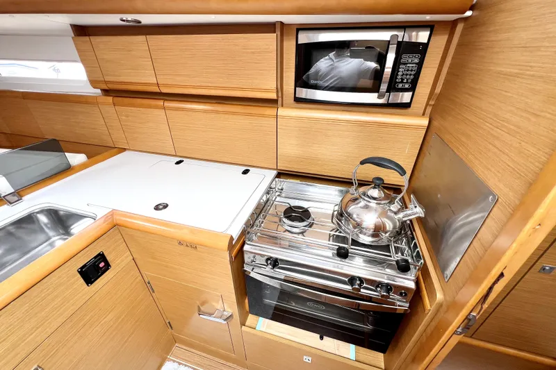 Knot Behaving Yacht Photos Pics 2014 Jeanneau Sun Odyssey 379 yacht kitchen with stove, microwave, and wooden cabinetry.