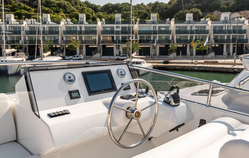 Yacht Photos Pics 2025 Sasga Yachts Menorquin 55 Flybridge helm with modern controls, docked near waterfront buildings.