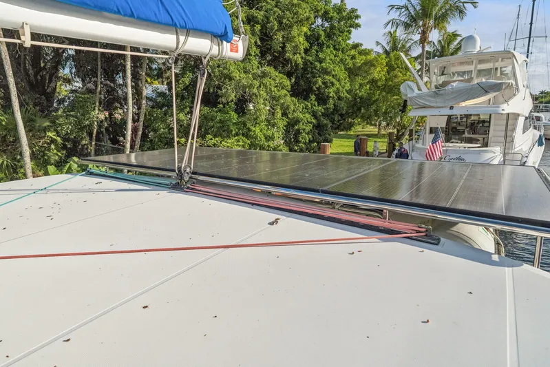 Benedetto Yacht Photos Pics 2020 Lagoon 42 catamaran with solar panels, docked near lush greenery and another yacht.