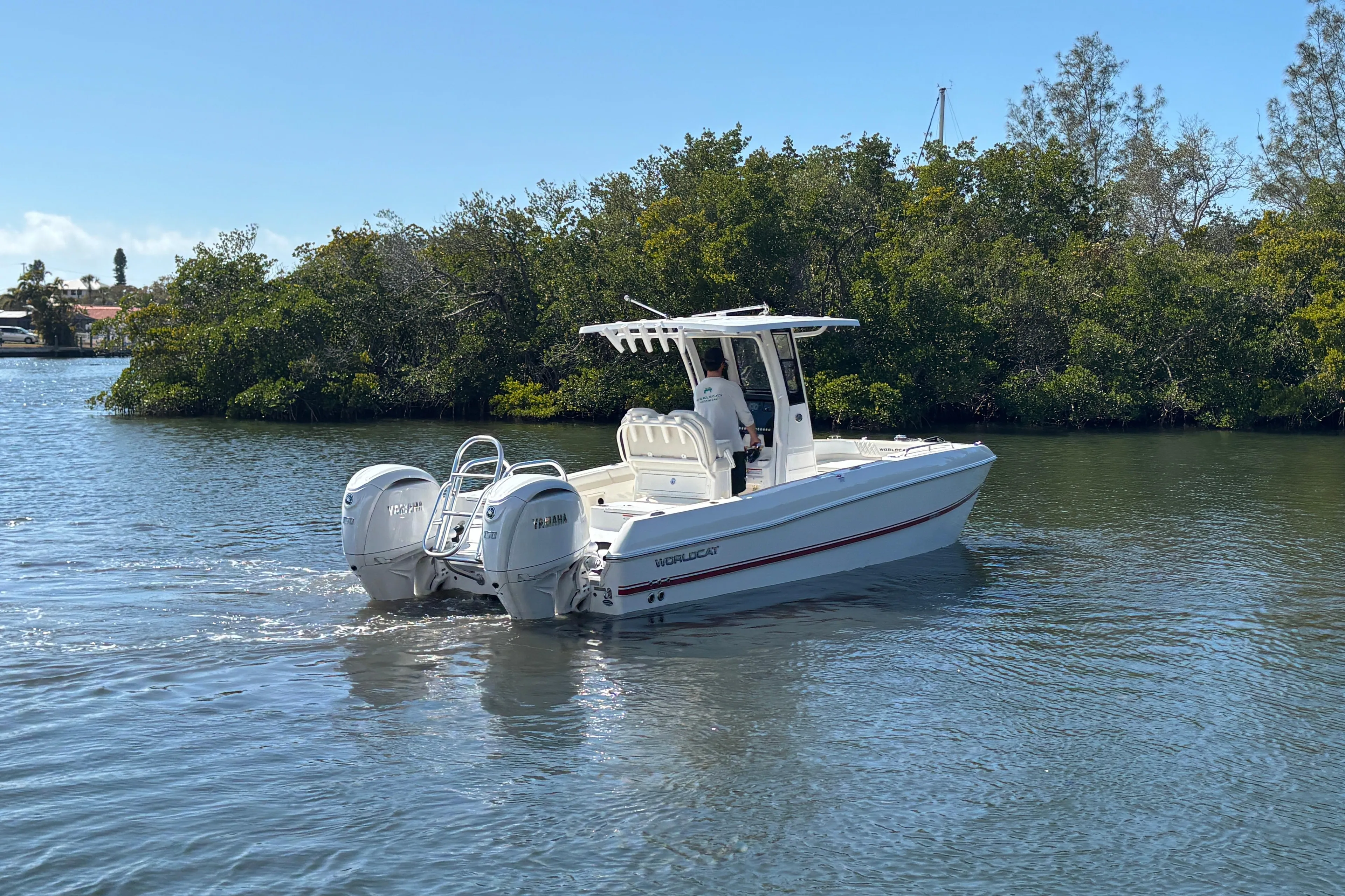 2026 World Cat 235 TE boat cruising on a calm river near lush greenery.