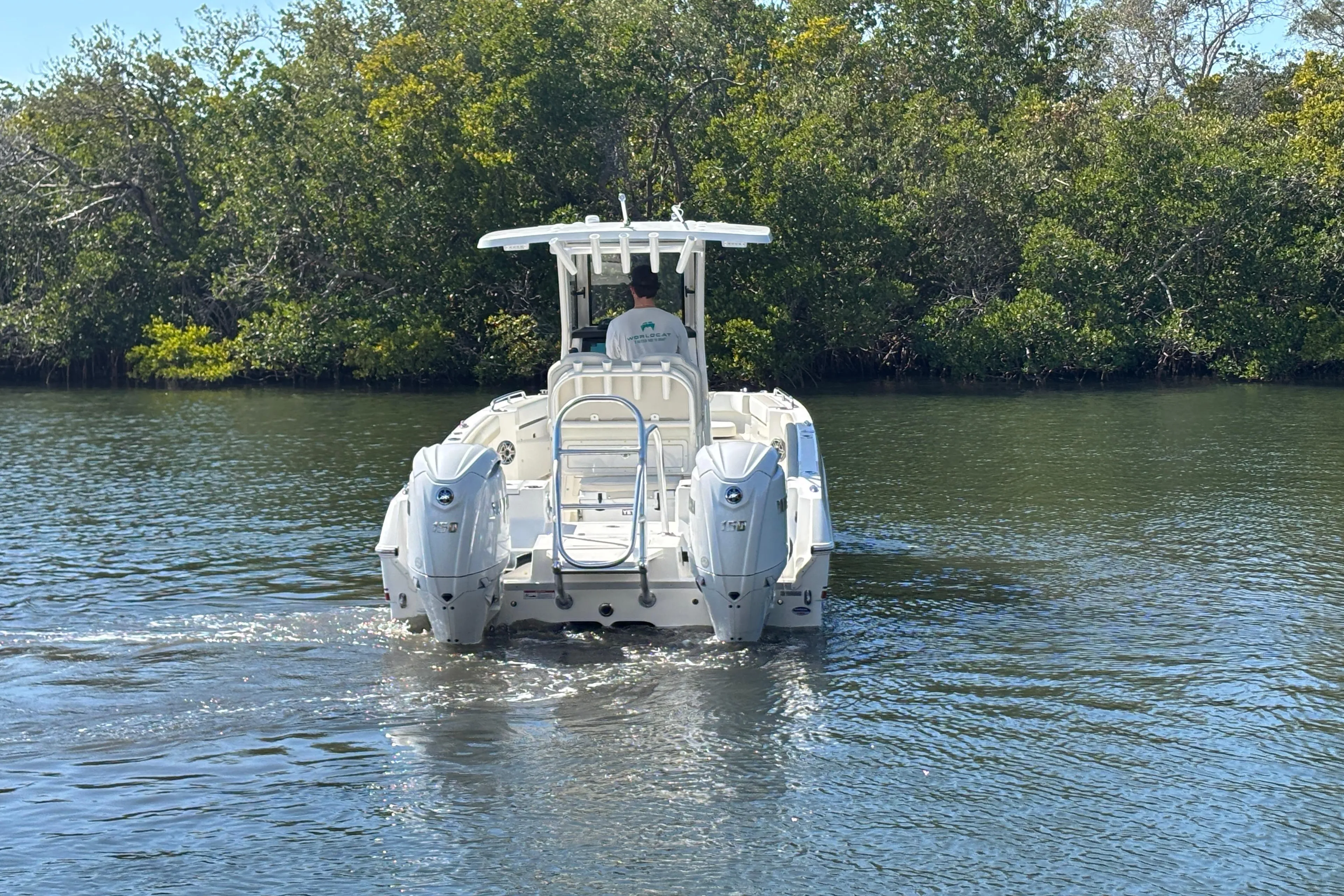 2026 World Cat 235 TE boat cruising on a calm river with lush greenery.