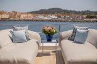 Luxurious yacht deck with elegant seating, floral arrangement, and scenic waterfront view. Custom Line 37, 2022.