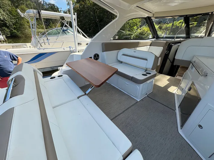 Wining Down Yacht Photos Pics Interior of 2016 Regal 35 Sport Coupe with seating and table, docked near another boat.