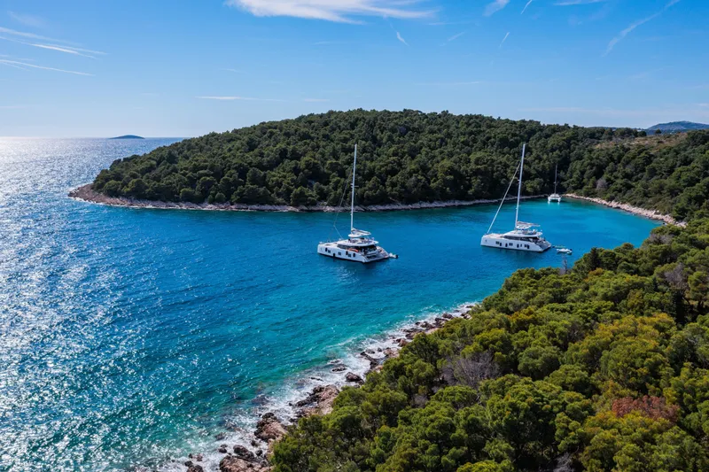 Mr.si Yacht Photos Pics Two Sunreef 60 Sailing yachts anchored in a serene, turquoise bay surrounded by lush greenery.