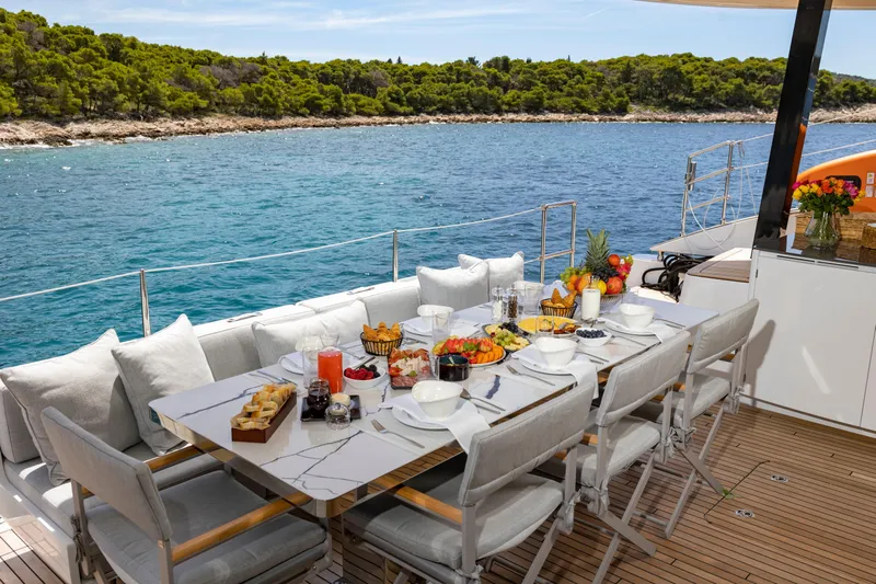 Mr.si Yacht Photos Pics Luxurious dining setup on 2023 Sunreef 60 Sailing yacht, overlooking serene ocean and lush coastline.
