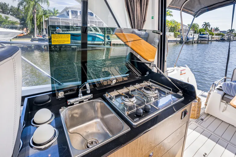  Yacht Photos Pics Outdoor kitchen on 2021 Beneteau Antares 9 yacht with sink and stove, docked by water.
