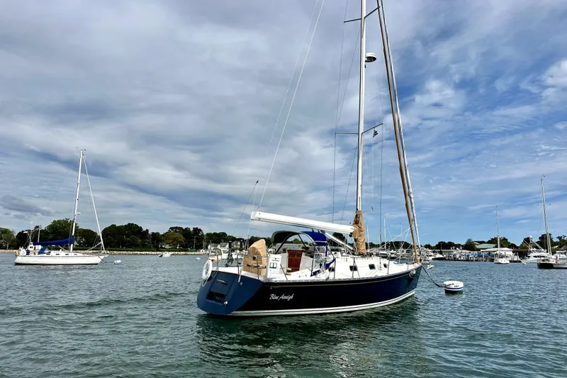 Blue Aweigh Yacht Photos Pics Sailboat Tartan 345, 2021 model, anchored in a serene harbor under a cloudy sky.