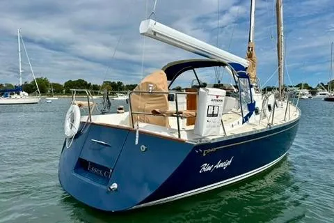 Blue Aweigh Yacht Photos Pics 2021 Tartan 345 sailboat, blue hull, docked in calm waters under a cloudy sky.