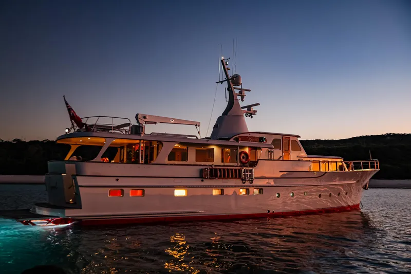 Kapal Yacht Photos Pics A 1971 Feadship yacht illuminated at dusk, reflecting on calm waters.