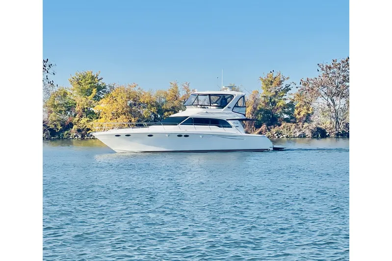 Nina Yacht Photos Pics 2002 Sea Ray 480 Sedan Bridge yacht cruising on a serene lake with autumn trees.