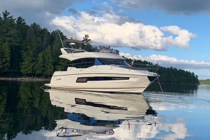Margie Yacht Photos Pics Luxurious 2018 Prestige 460 yacht on serene lake, reflecting clear blue sky and clouds.