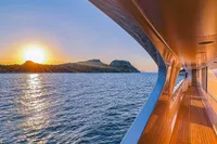 Luxurious 2008 Benetti Custom yacht at sunset, cruising near scenic islands.