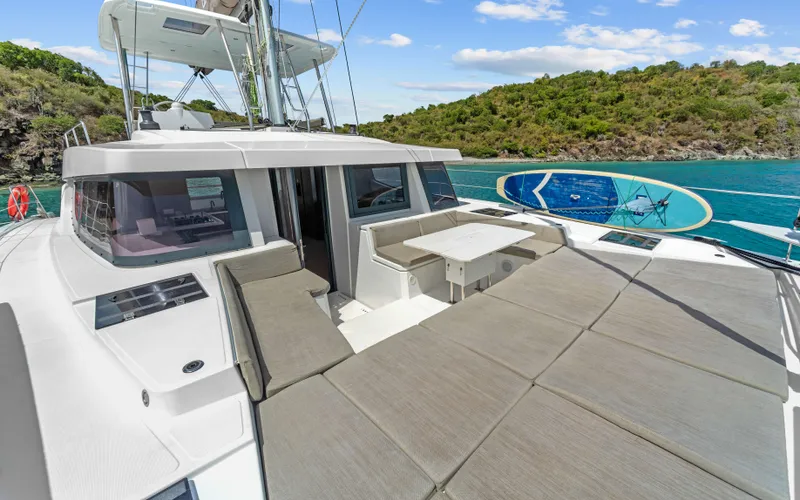Always Sunday Yacht Photos Pics 2022 Bali 4.8 catamaran with sunbathing area, table, and paddleboard, anchored near lush island.