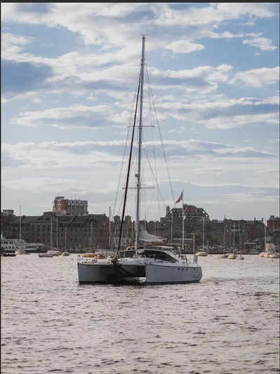 Blue Star Yacht Photos Pics Sailing catamaran Privilege 43, 1993 model, on a calm waterway with cityscape background.