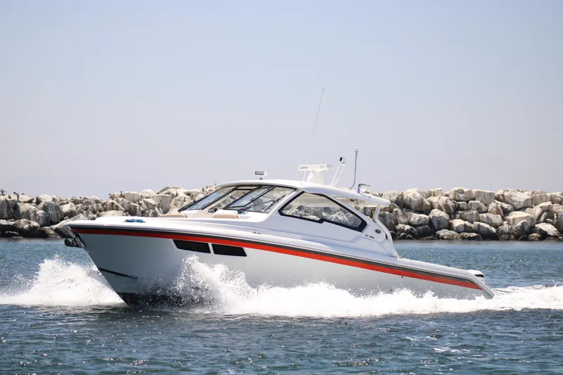 Flawless Seas Yacht Photos Pics 2019 Pursuit DC 365 Dual Console boat cruising on water near rocky shoreline.