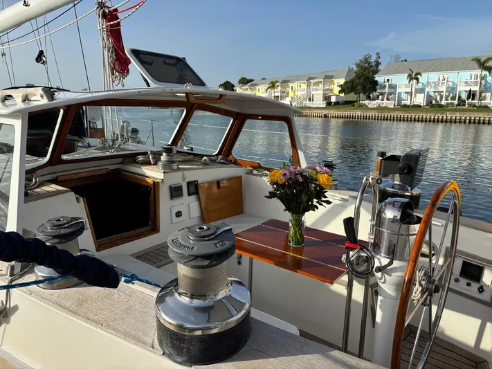 Colleen Yacht Photos Pics Sailboat cockpit with wooden steering wheel, flowers on table, and waterfront view. Cambria 44/46, 1984.