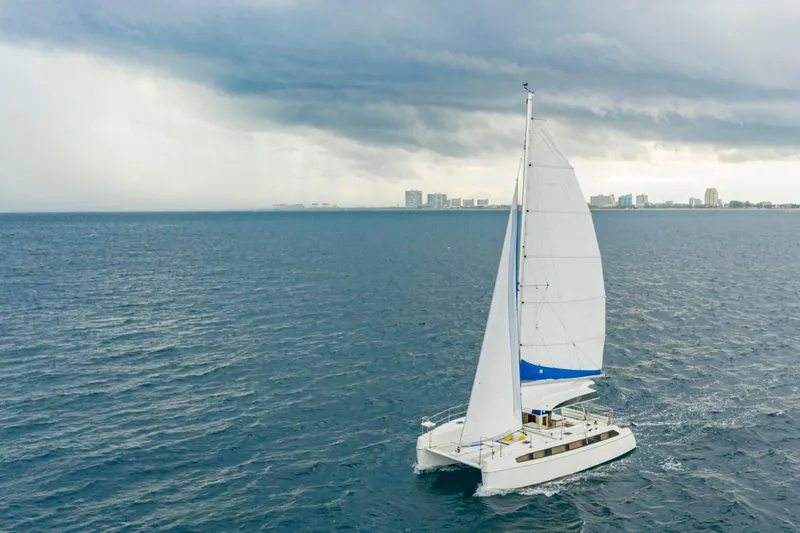  Yacht Photos Pics Sailing catamaran on open sea under cloudy skies, near city skyline.