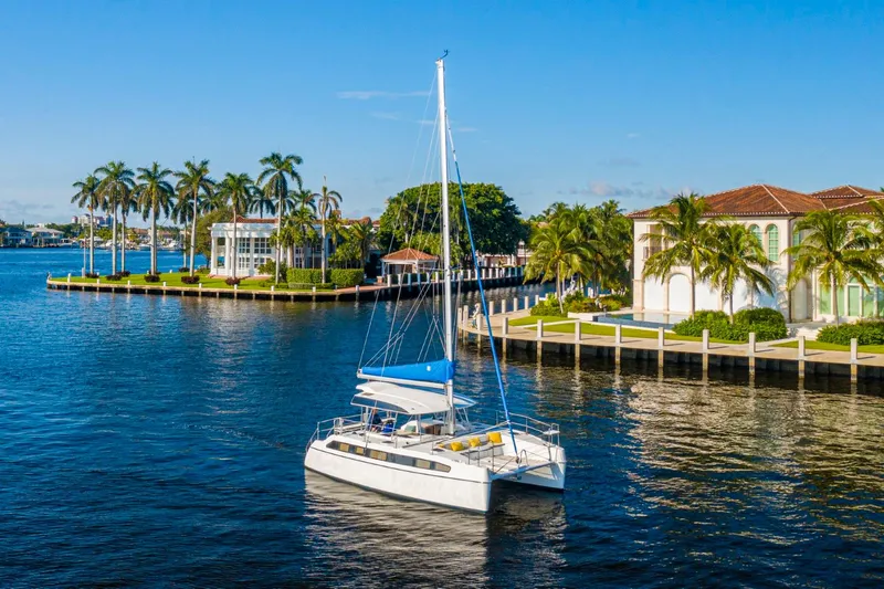  Yacht Photos Pics A 2025 Smart Cat S280 catamaran sailing near luxurious waterfront homes and palm trees.
