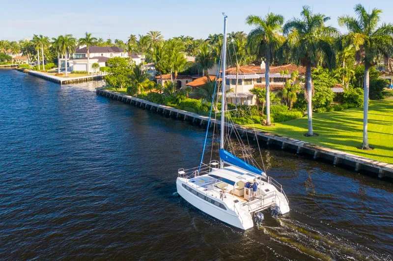  Yacht Photos Pics Catamaran sailing on a sunny canal near luxury waterfront homes and palm trees.