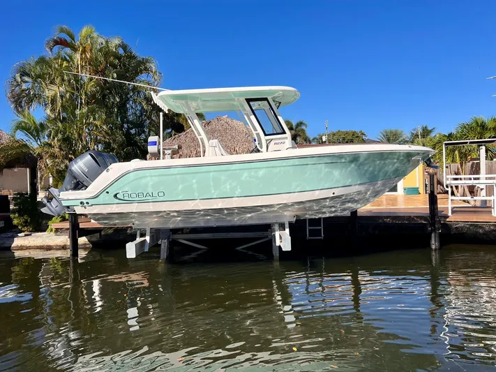  Yacht Photos Pics 2021 Robalo 272 boat docked on a sunny day, surrounded by lush greenery.