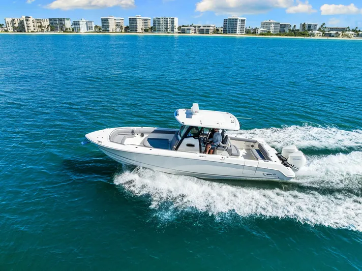  Yacht Photos Pics 2022 Boston Whaler 330 Outrage cruising on blue ocean near coastal buildings.