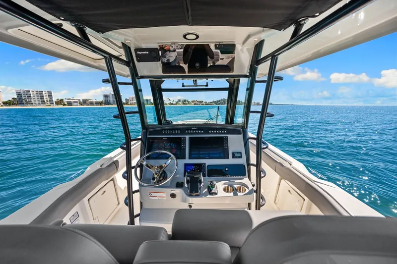  Yacht Photos Pics Boston Whaler 330 Outrage 2022 helm view, navigating clear blue waters near coastal buildings.