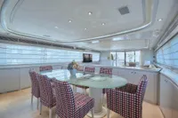 Luxurious yacht interior with modern dining area, glass table, patterned chairs, and large windows. Custom Line 112, 2005.
