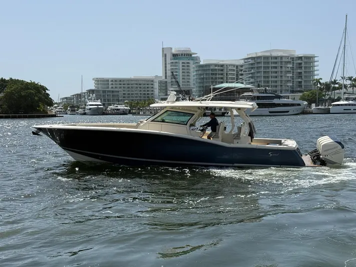 Reel Patience Yacht Photos Pics 2019 Scout 420 LXF boat cruising in a marina with modern buildings in the background.