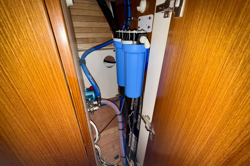 Nereid Yacht Photos Pics Water filtration system inside 2020 Catalina 425 yacht, featuring blue filter and wooden cabinetry.