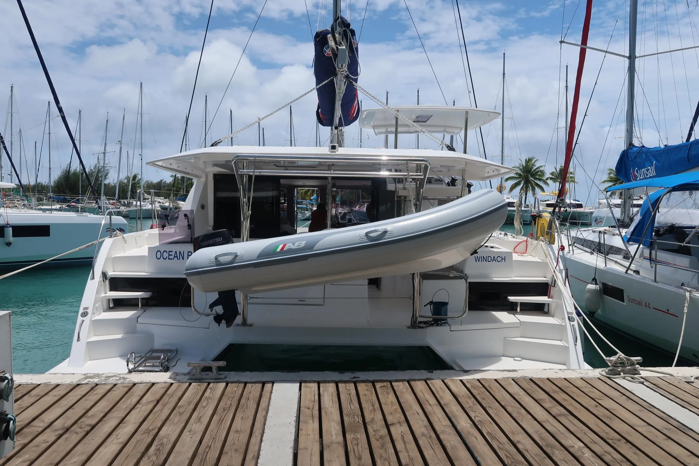 2019 Leopard 40 catamaran docked with dinghy, surrounded by sailboats, under a partly cloudy sky.